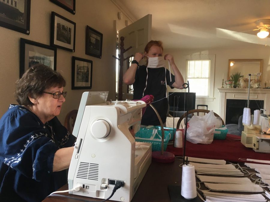 Linda Floyd (left) sews the two pieces of cloth together to make the base of the mask. Mary Katherine Lawrence (right) tests out the sizing on her face. 
Photo by Hannah Denham.