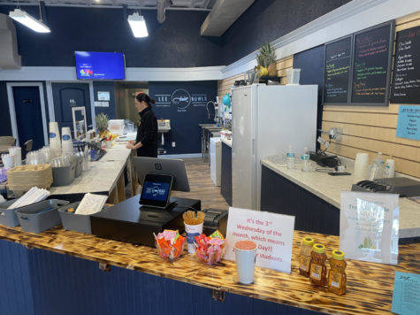 Inside local Lexington business, with woman in black behind a counter preparing an acai bowl. Chalkboards line the walls behind the counter with neon menu options.