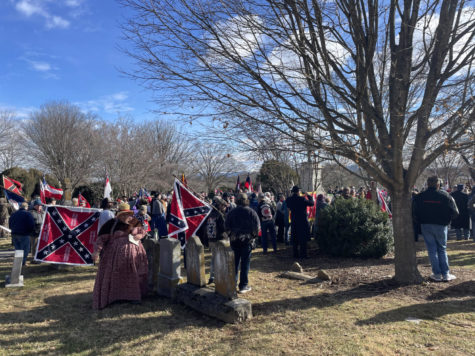 A group of people carrying Confederate flags and symbols are assembled in a cemetery.