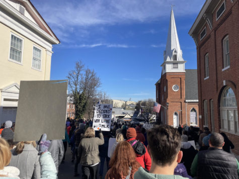 A crowd of people carrying signs march down a downtown street near a church.