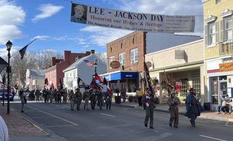 People wearing Confederate army regalia march under a banner reading partly, "Lee-Jackson Day, Honoring Our History & Heritage"