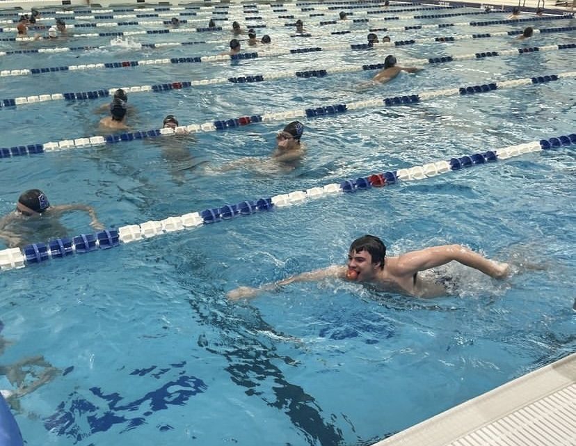 A man swims in a pool while other people tread water in the background.