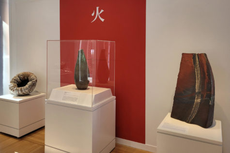 Three artworks, from left a circular white piece with a dent in the middle, then a tall swirling oblong vase, then a large textured slab with a curved vertical slice in it. The artworks sit next to a gallery wall.