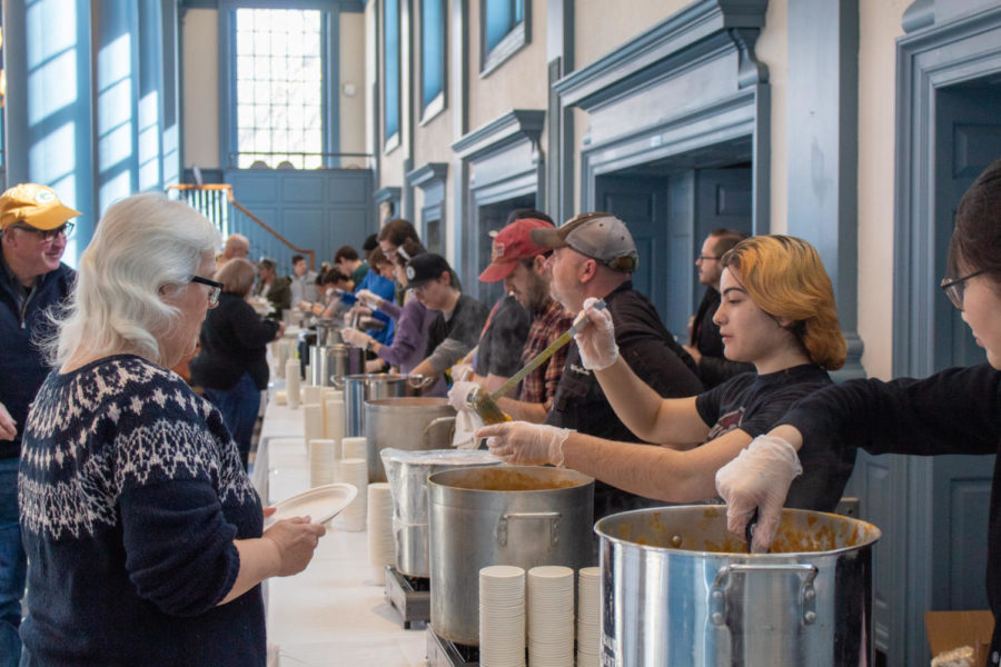 People line up, while others serve soup from large pots.