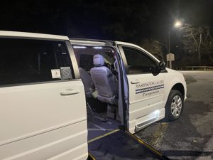 A van has its sliding passenger door open. A wheelchair ramp extends from the door to the ground.