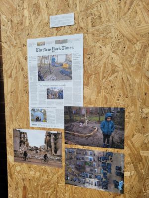 A plywood wall has photos and newspaper pages on it.