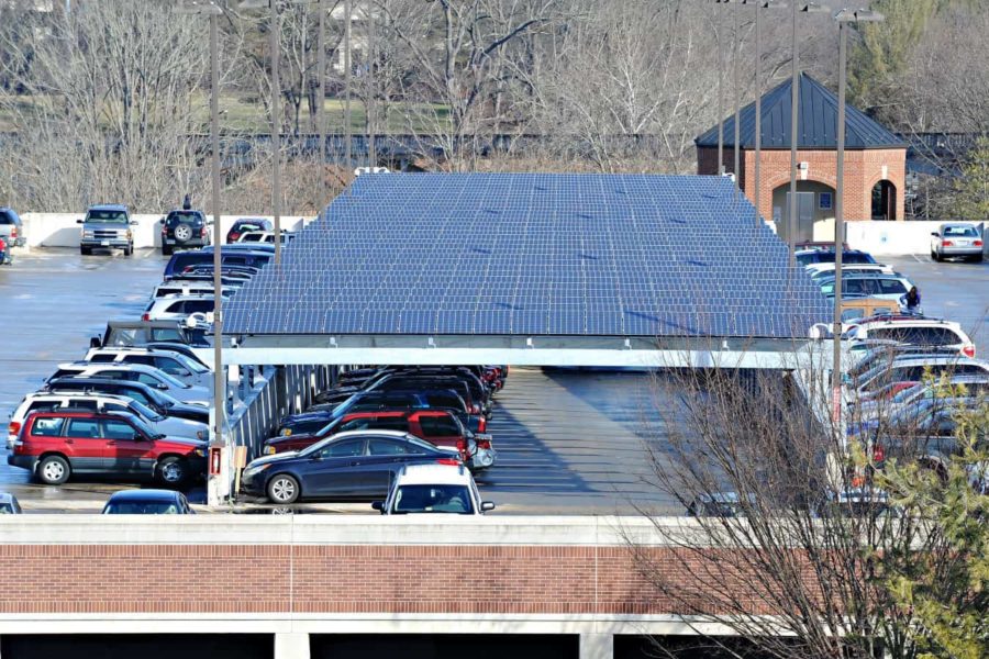 Many rows of solar panels form a cover over the middle portion of a parking garage top floor.