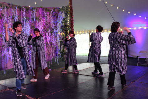 A group of students dance, walking in a line. They are wearing blue and white patterned Japanese robes.