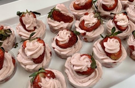 A tray full of pink whipped mousse cups, with strawberries on top.