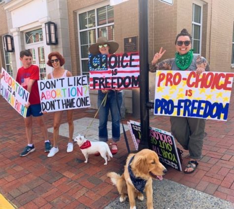 Three women and one man hold signs supporting abortion rights and stand on a street corner. Two dogs are also present.