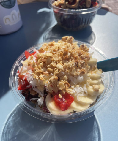 An acai bowl, topped with banana slices, red fruit and granola. The bowl sits on a table.